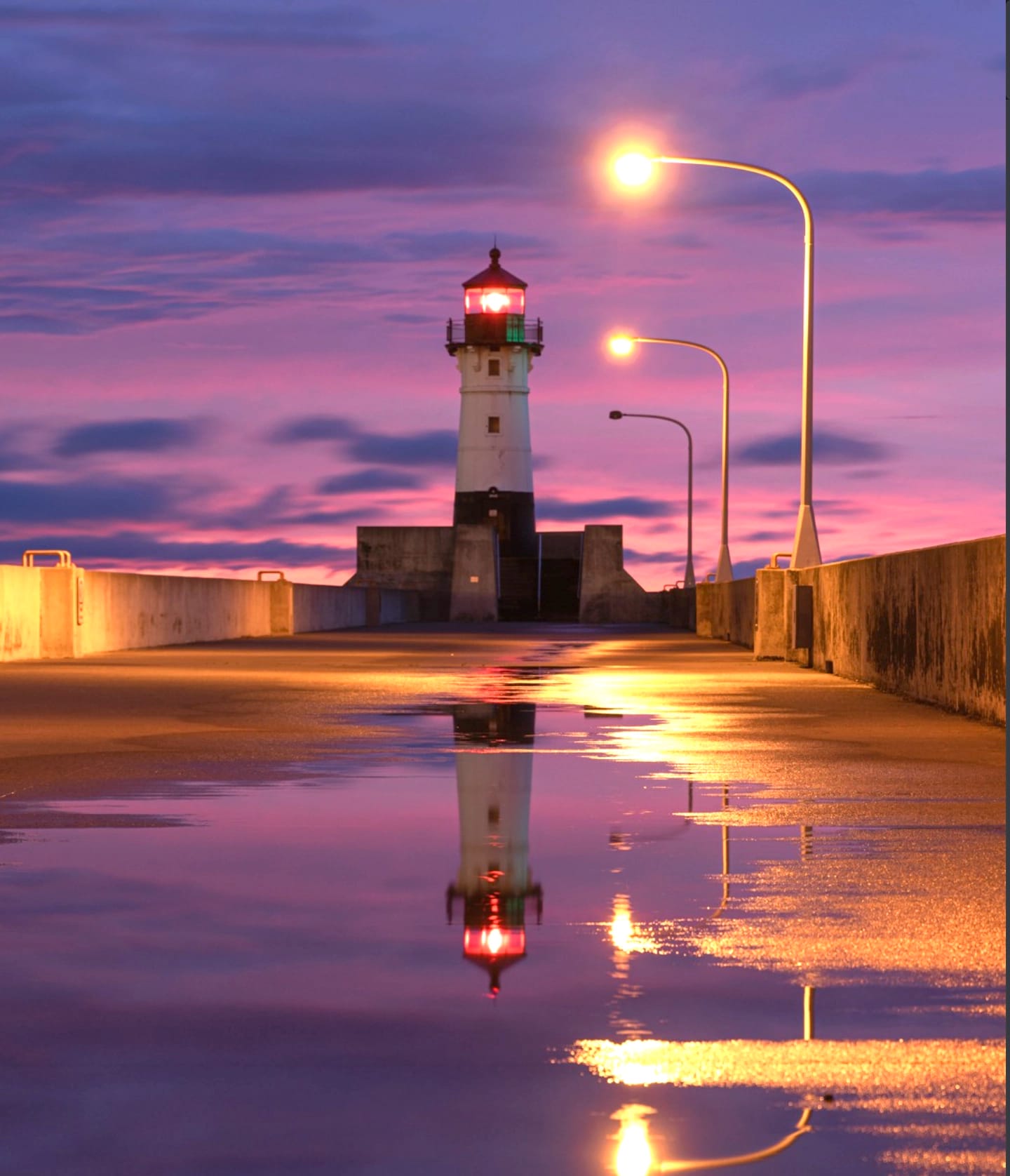 A lighthouse at daybreak in a dense pink fog melting into its own reflection and purple ambiance.